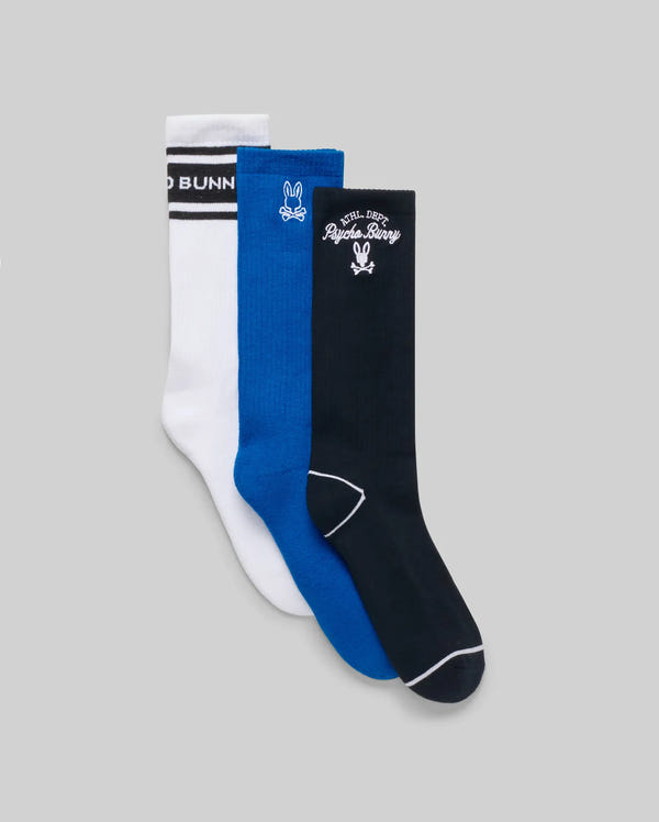 The Psycho Bunny MENS 3 PACK SPORT SOCK (MO2200006) includes three pairs—white with black stripes and text, solid blue, and black with vintage motifs—crafted from soft Pima cotton and shown side by side on a neutral gray background.