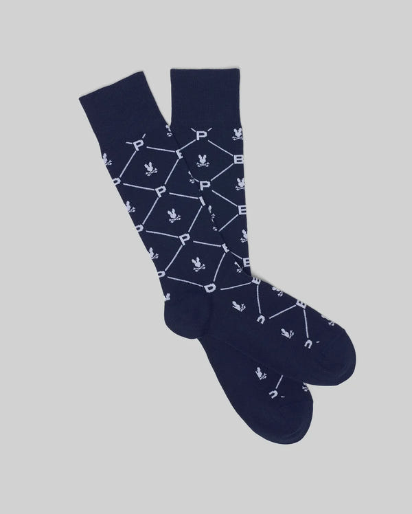The Psycho Bunny MENS NEW ALL OVER DRESS SOCK (MO2200007) in navy blue is crafted from soft Pima cotton, featuring white hexagons, “P” letters, and fleur-de-lis—ideal for formalwear. Shown on a light gray background.