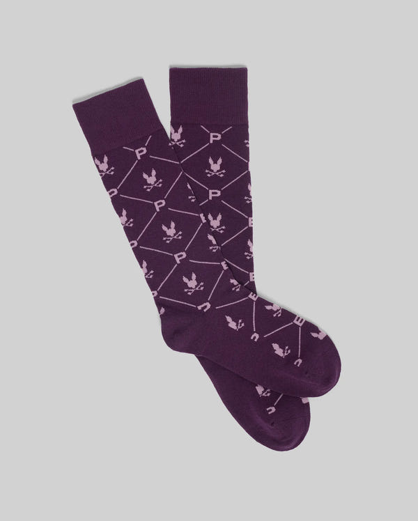 The Psycho Bunny MENS NEW ALL OVER BUNNY DRESS SOCK (MO2200007) features purple premium Pima cotton with white geometric lines, "P" and "U" letters, and leaf-like motifs, shown flat on a light gray background.