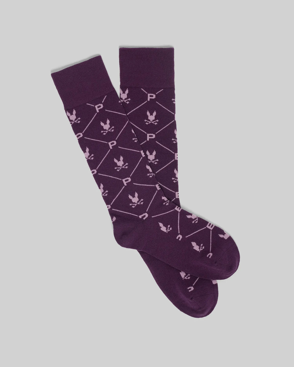 The Psycho Bunny MENS NEW ALL OVER BUNNY DRESS SOCK (MO2200007) features purple premium Pima cotton with white geometric lines, "P" and "U" letters, and leaf-like motifs, shown flat on a light gray background.
