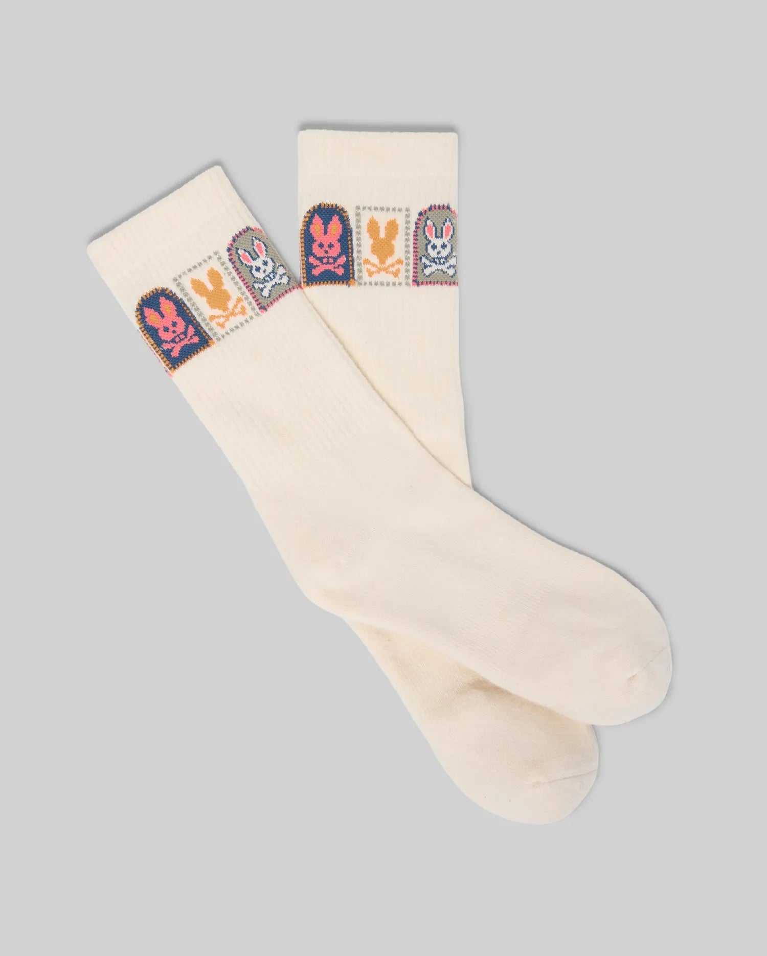 The Psycho Bunny MENS SUNDEW GRAPHIC SPORT SOCK (MO2200020) features cream-colored Pima cotton with colorful cartoon bunny graphics in squares near the top, shown laid flat on a plain gray background.