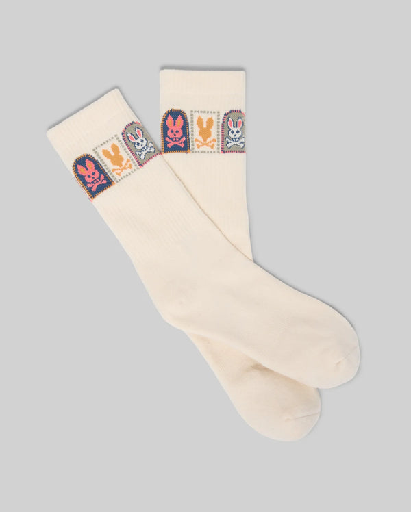 The Psycho Bunny MENS SUNDEW GRAPHIC SPORT SOCK (MO2200020) features cream-colored Pima cotton with colorful cartoon bunny graphics in squares near the top, shown laid flat on a plain gray background.