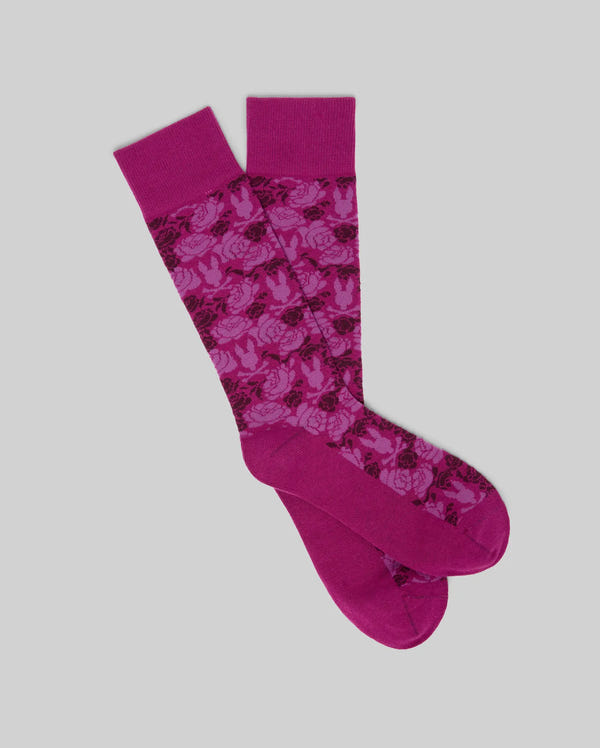 The Psycho Bunny MENS FLORAL BUNNY DRESS SOCK - MO2200021 features a magenta floral pattern with solid magenta toes, heels, and cuffs, shown against a light gray background.