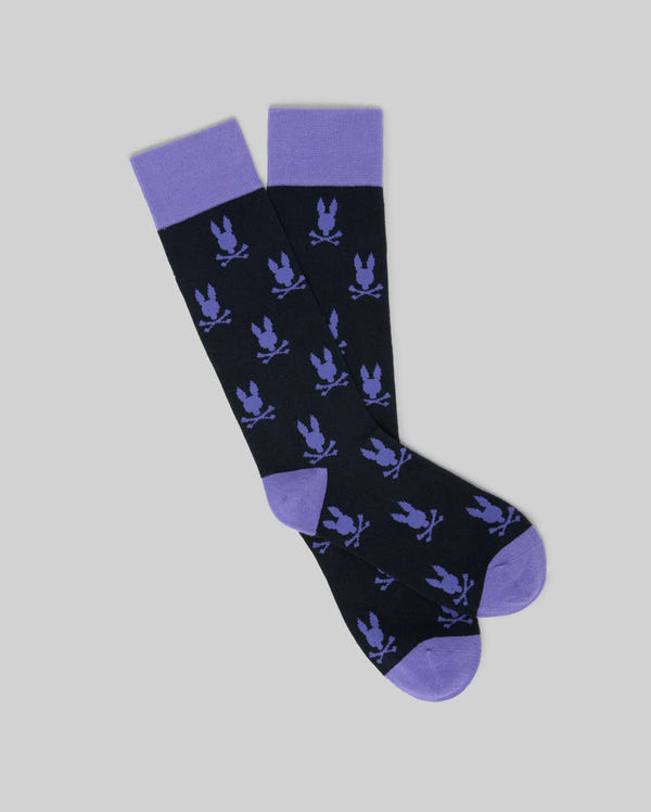 The Psycho Bunny MENS ALL OVER BUNNY DRESS SOCK (MO2200022) features a black base with purple cuffs, heels, toes, and all-over purple bunny motifs, shown on a light gray background.