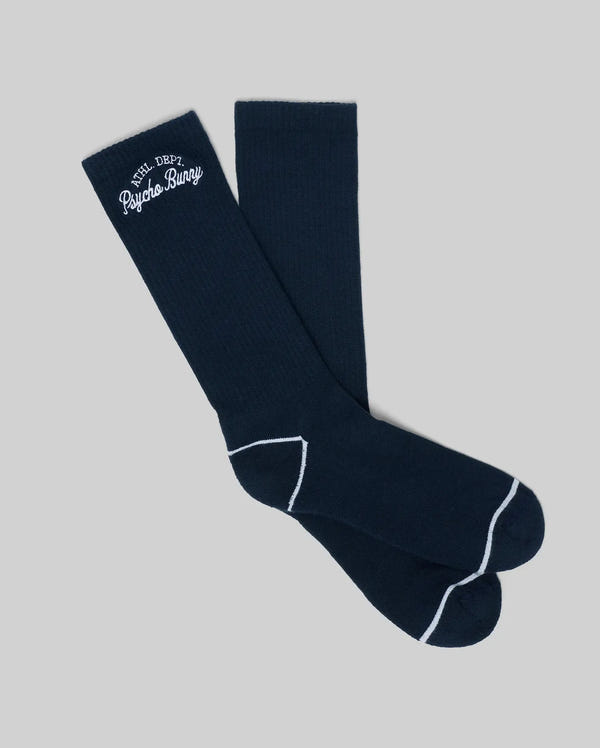 The MENS SCPRIT SOCKS - MO2200035 by Psycho Bunny are navy blue crew socks in soft Pima cotton, featuring white toe and heel trim and an "ATH DEPT. Psycho Bunny" embroidered logo. Shown flat on a light gray background.