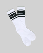 The Psycho Bunny MENS 2 PACK SPORT SOCK (MO2200037) features white cotton crew socks with black stripes and "BAD BUNNY" text on the band, shown on a gray background—ideal for sporty style and comfort.