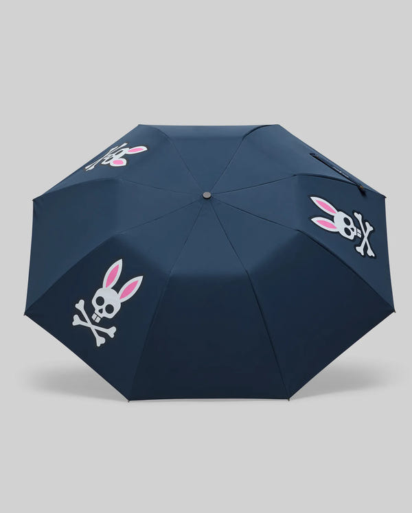 The Psycho Bunny MENS UMBRELLA BUNNY LOGO - MO2400021 is a navy blue umbrella with white skull and crossbones each featuring pink bunny ears, shown against a gray background. Made in China.