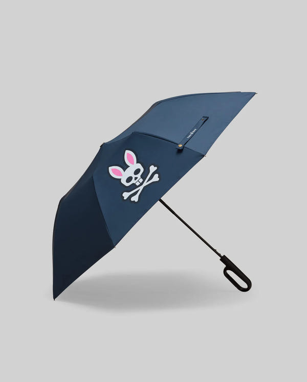 The Psycho Bunny MENS UMBRELLA BUNNY LOGO (MO2400021) features a navy canopy with a white skull and crossbones graphic sporting pink bunny ears on one panel, photographed on a plain light gray background. Made in China.