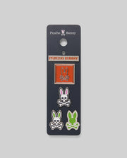 The Psycho Bunny MENS PINS BUNDLE - MO2400051 includes four vibrant pins on a navy card: one orange rectangle pin with the bunny-and-crossbones, plus three bunny head pins in orange, purple, and green.