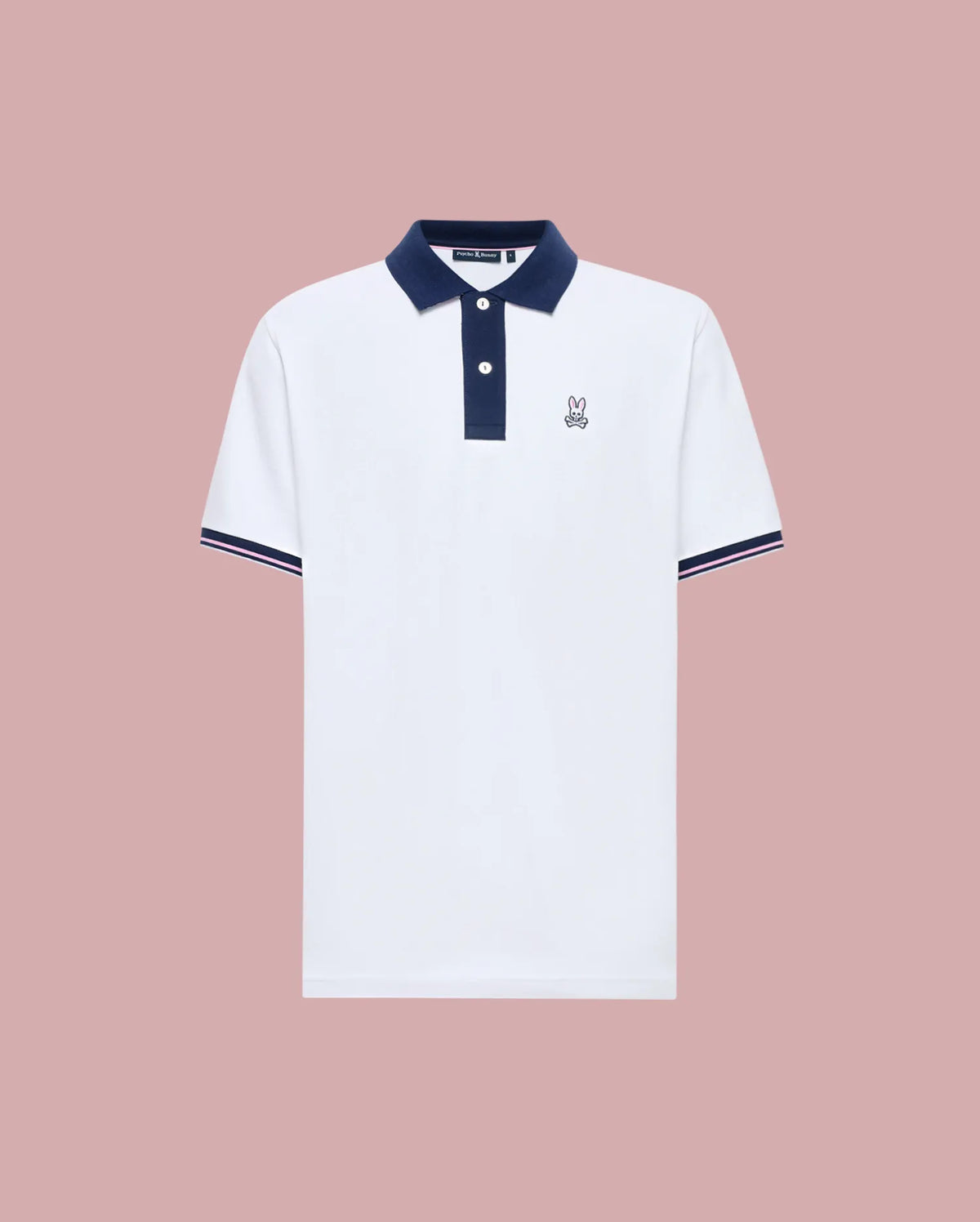 The Psycho Bunny MENS ARCHIVE CLASSIC BUNNY PIQUE POLO (MT0100010) is a white Pima cotton short-sleeve polo with a navy collar, placket, and sleeve trim, plus an embroidered Bunny logo on the left chest. Shown against a muted pink background.