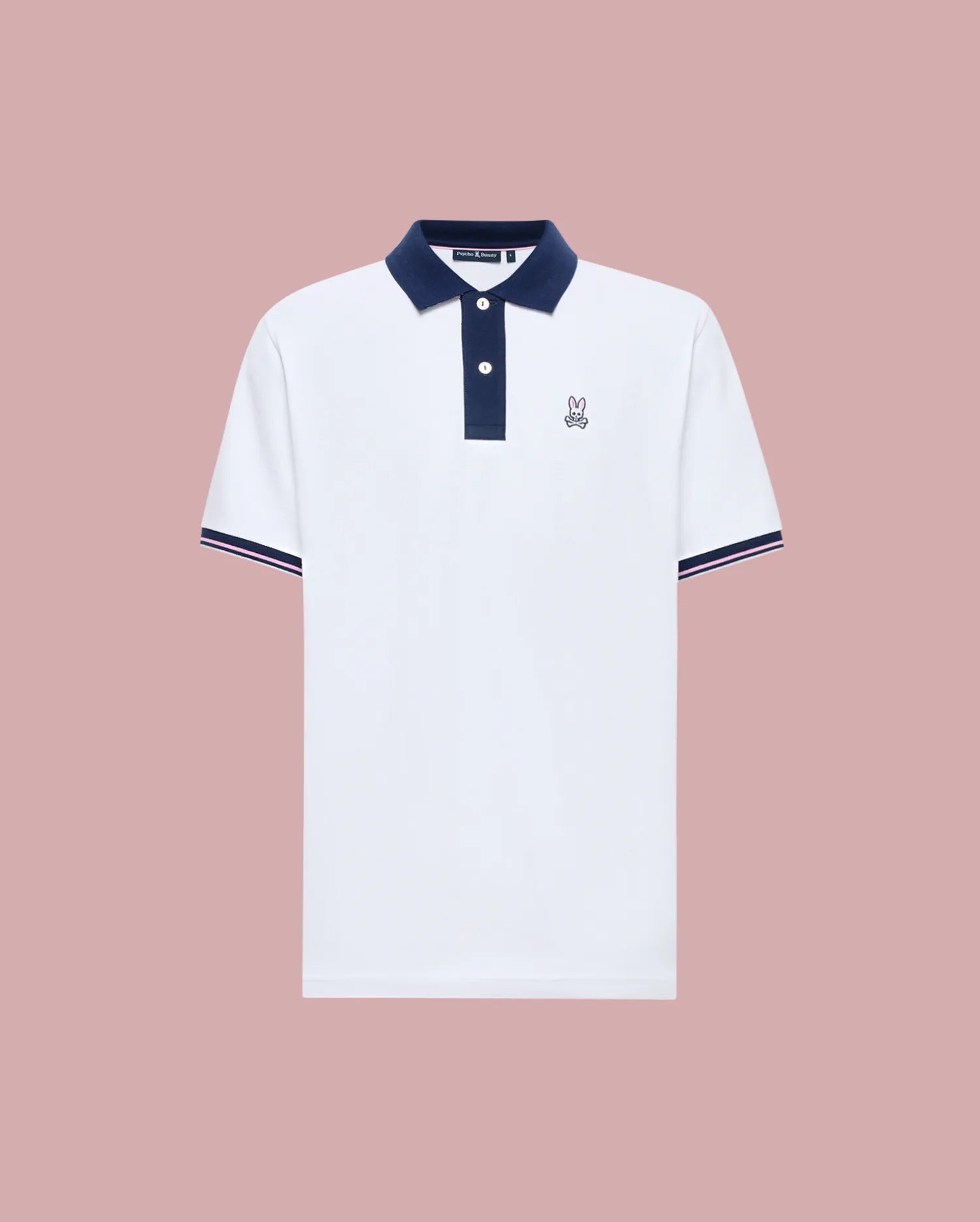 The Psycho Bunny MENS ARCHIVE CLASSIC BUNNY PIQUE POLO (MT0100010) is a white Pima cotton short-sleeve polo with a navy collar, placket, and sleeve trim, plus an embroidered Bunny logo on the left chest. Shown against a muted pink background.