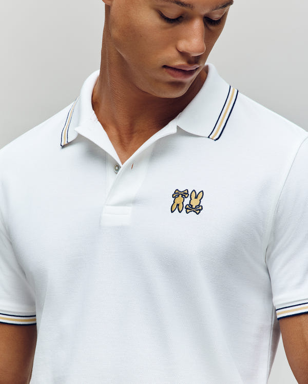 A man looks down while wearing the Psycho Bunny MENS ARCHIVE NEON BUNNY POLO (MT0100018), a soft Pima cotton knit shirt with thin blue and yellow collar stripes and an embroidered Bunny plus another cartoon animal on the chest.
