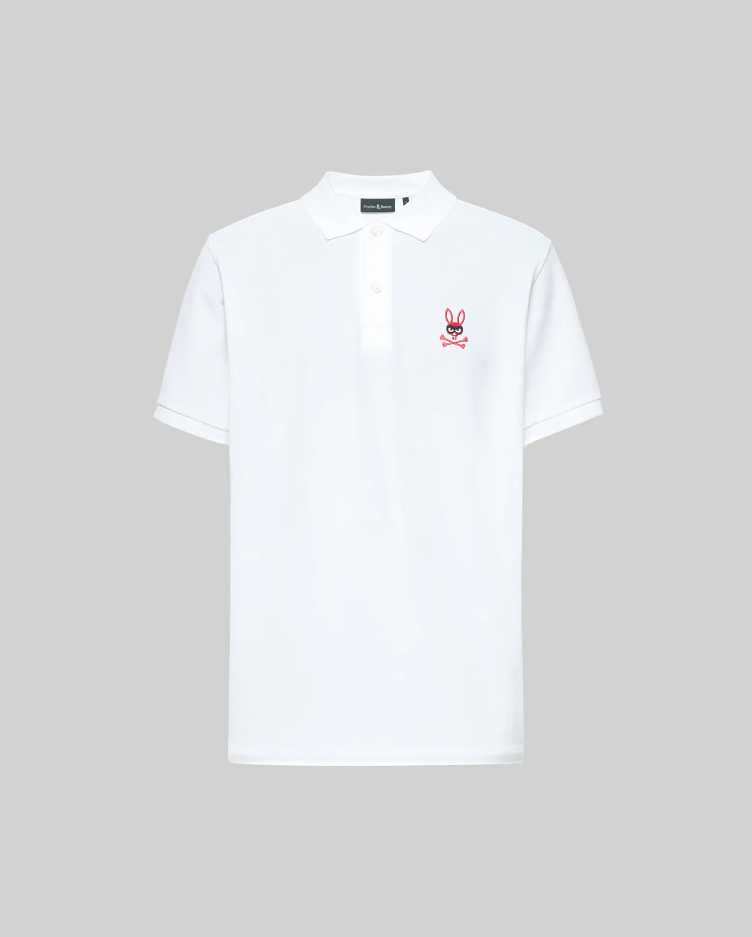 The Psycho Bunny MENS MISCHIEF BUNNY PIQUE POLO (MT0100025) is a white short-sleeve polo with a collar, three mother-of-pearl buttons, and a small pink bunny logo with crossbones on the left chest. Background is plain light gray.