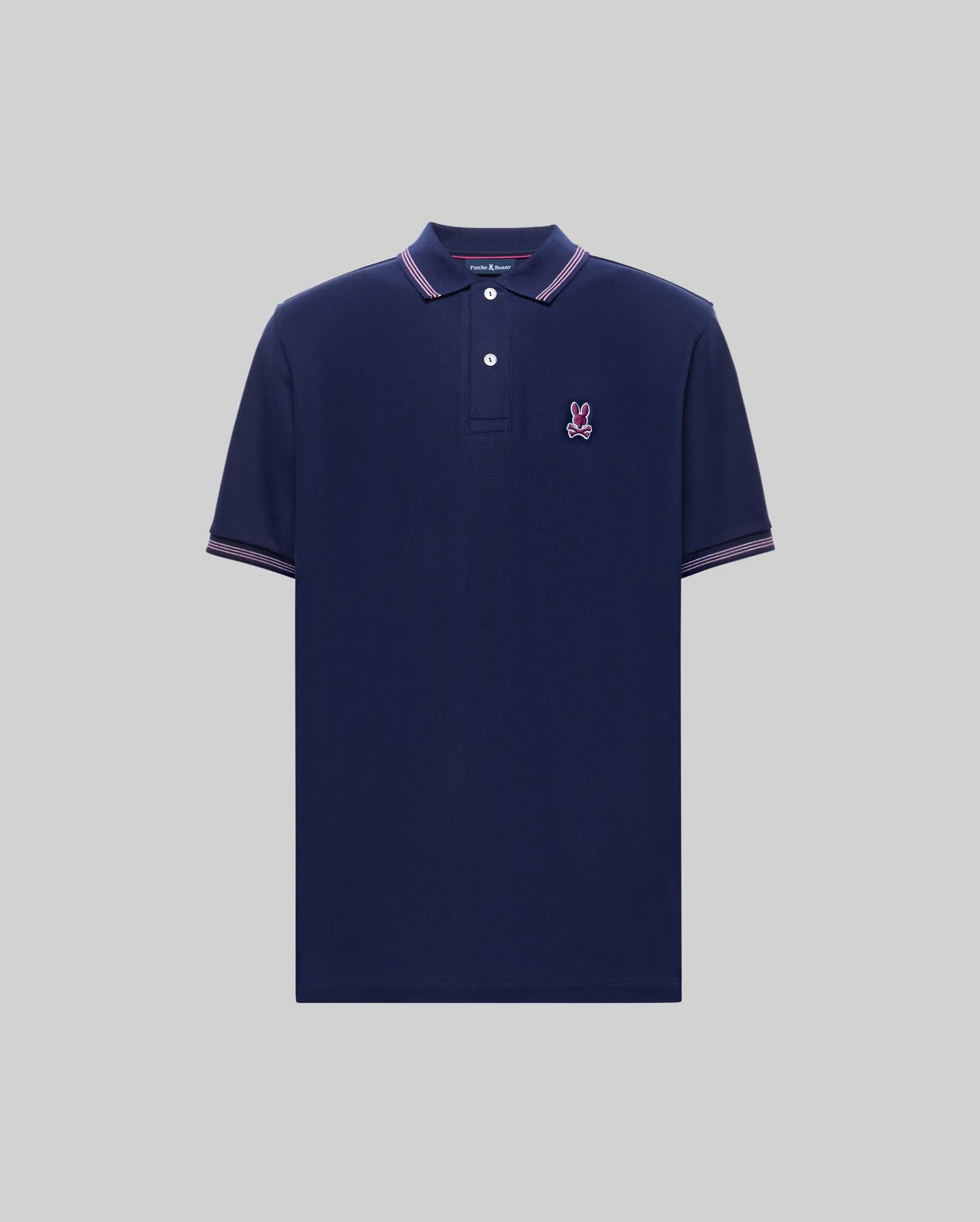 The Psycho Bunny MENS HART PIQUE POLO SHIRT (MT0100032) features a modern fit in navy blue, short sleeves, pink/white/navy striped collar and sleeve trim, an embroidered bunny logo on the chest, and soft Pima cotton. Displayed on gray.