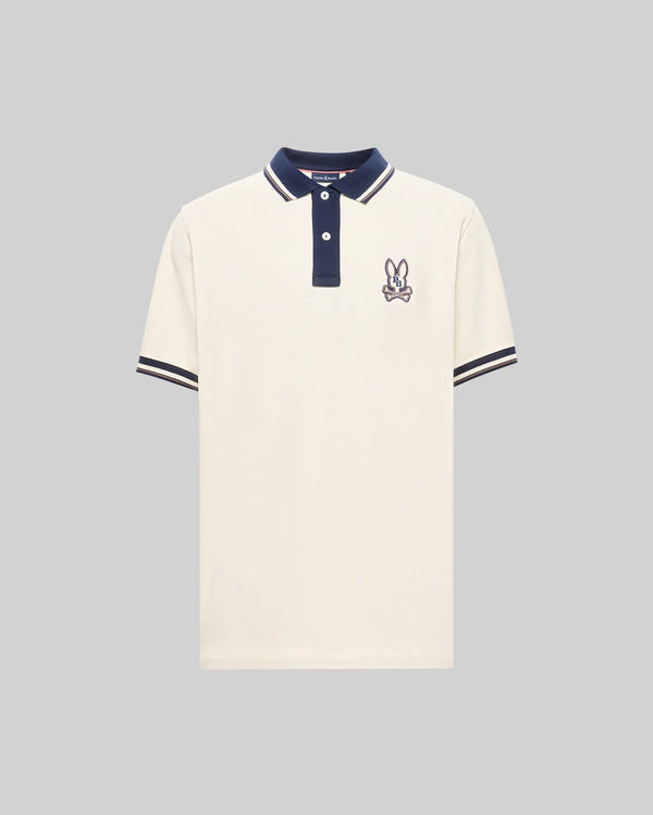 The Psycho Bunny MENS WADE PIQUE POLO SHIRT - MT0100044 is a white Pima cotton polo with navy collar and sleeve trim, featuring a small embroidered bunny logo on the left chest, shown on a light gray background.