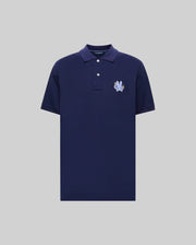 The Psycho Bunny MENS AUGUSTE PIQUE POLO SHIRT (MT0100051) is a navy blue short-sleeve Pima cotton polo with a collar, two white buttons, and a light blue embroidered crest on the left chest, shown on a light gray background.