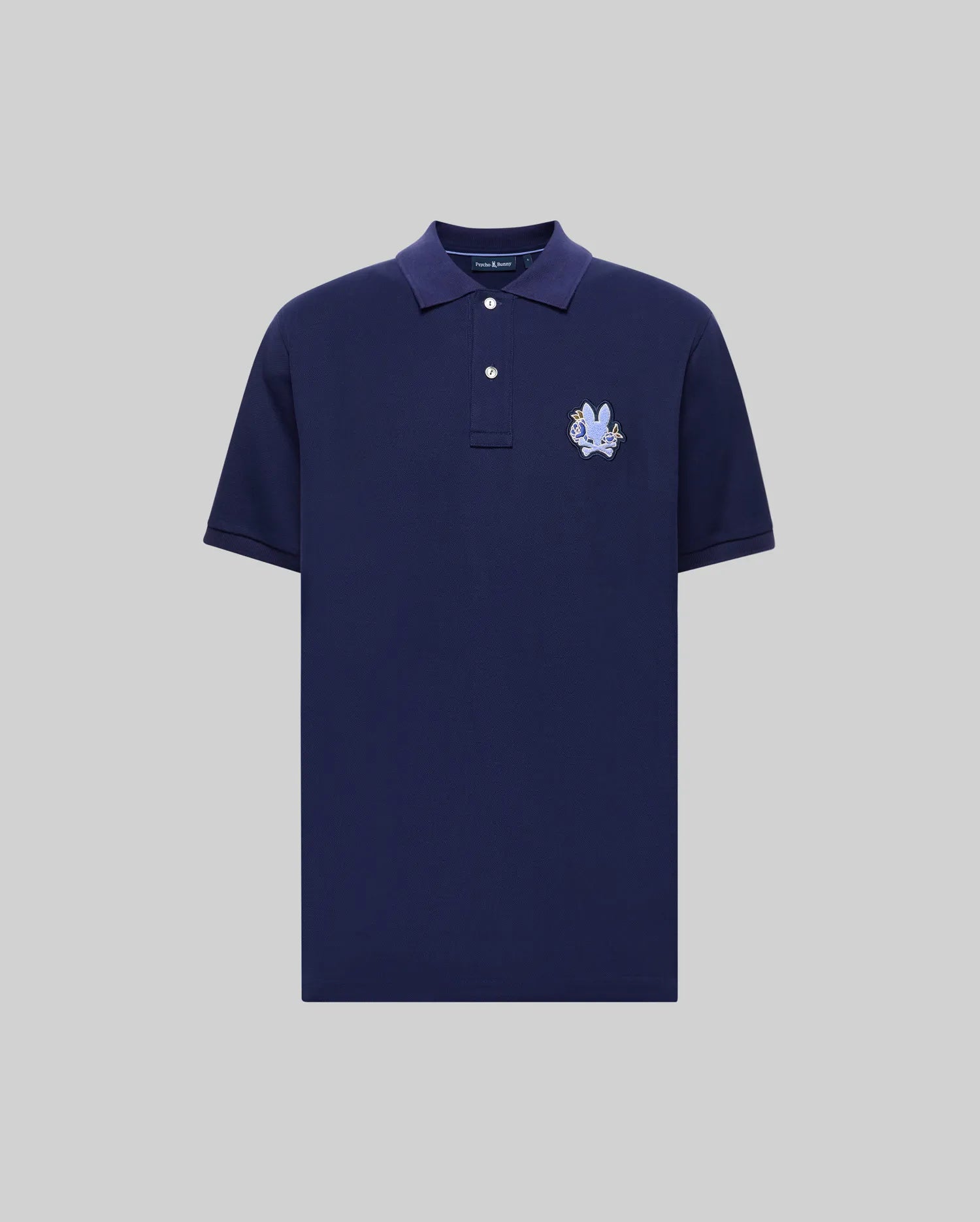 The Psycho Bunny MENS AUGUSTE PIQUE POLO SHIRT (MT0100051) is a navy blue short-sleeve Pima cotton polo with a collar, two white buttons, and a light blue embroidered crest on the left chest, shown on a light gray background.