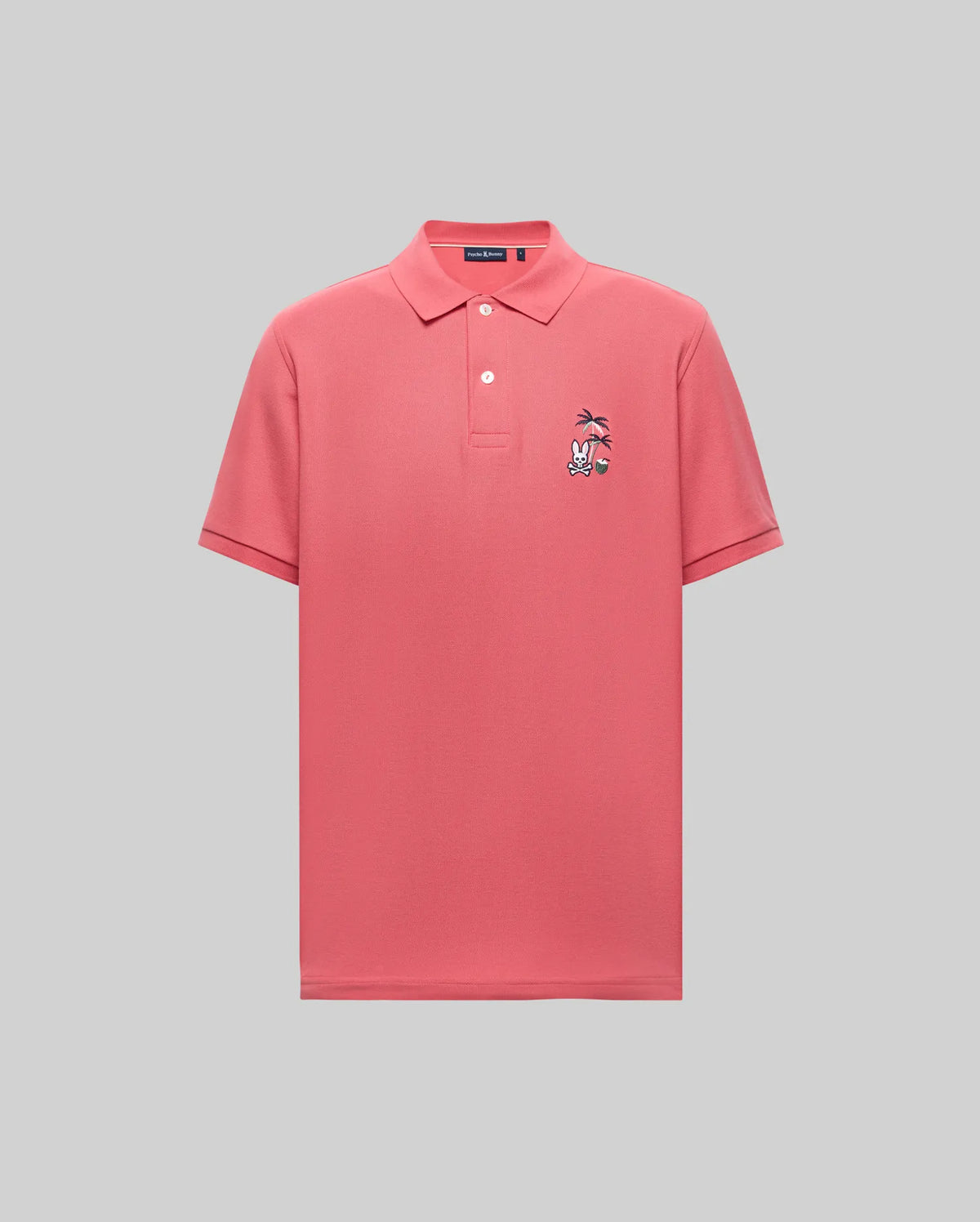 The Psycho Bunny MENS SONNY PIQUE POLO (MT0100094) is a coral pink Pima cotton short-sleeve polo with a collar, three buttons, and a small cartoon chest embroidery on the left, shown on a light gray background.