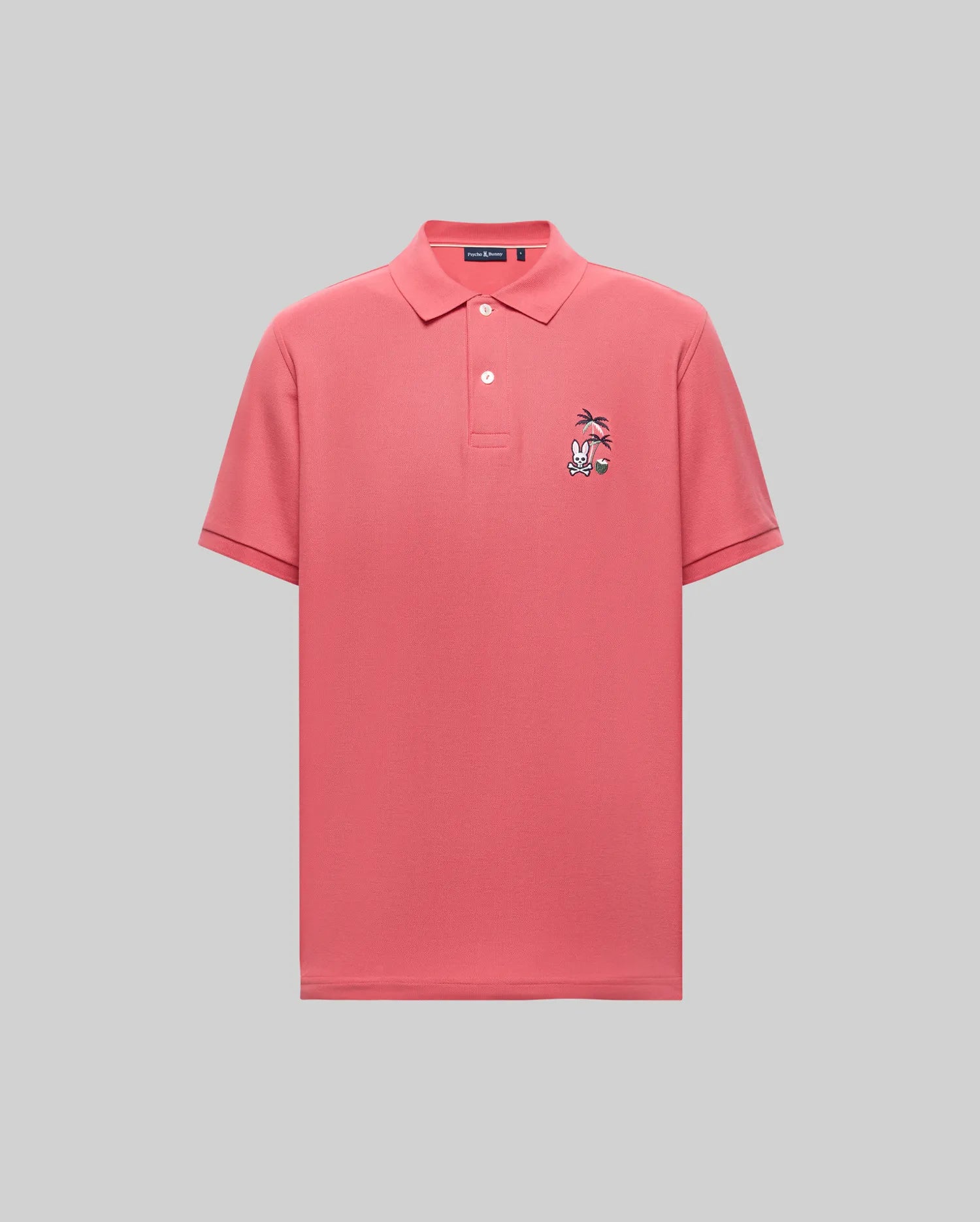 The Psycho Bunny MENS SONNY PIQUE POLO (MT0100094) is a coral pink Pima cotton short-sleeve polo with a collar, three buttons, and a small cartoon chest embroidery on the left, shown on a light gray background.