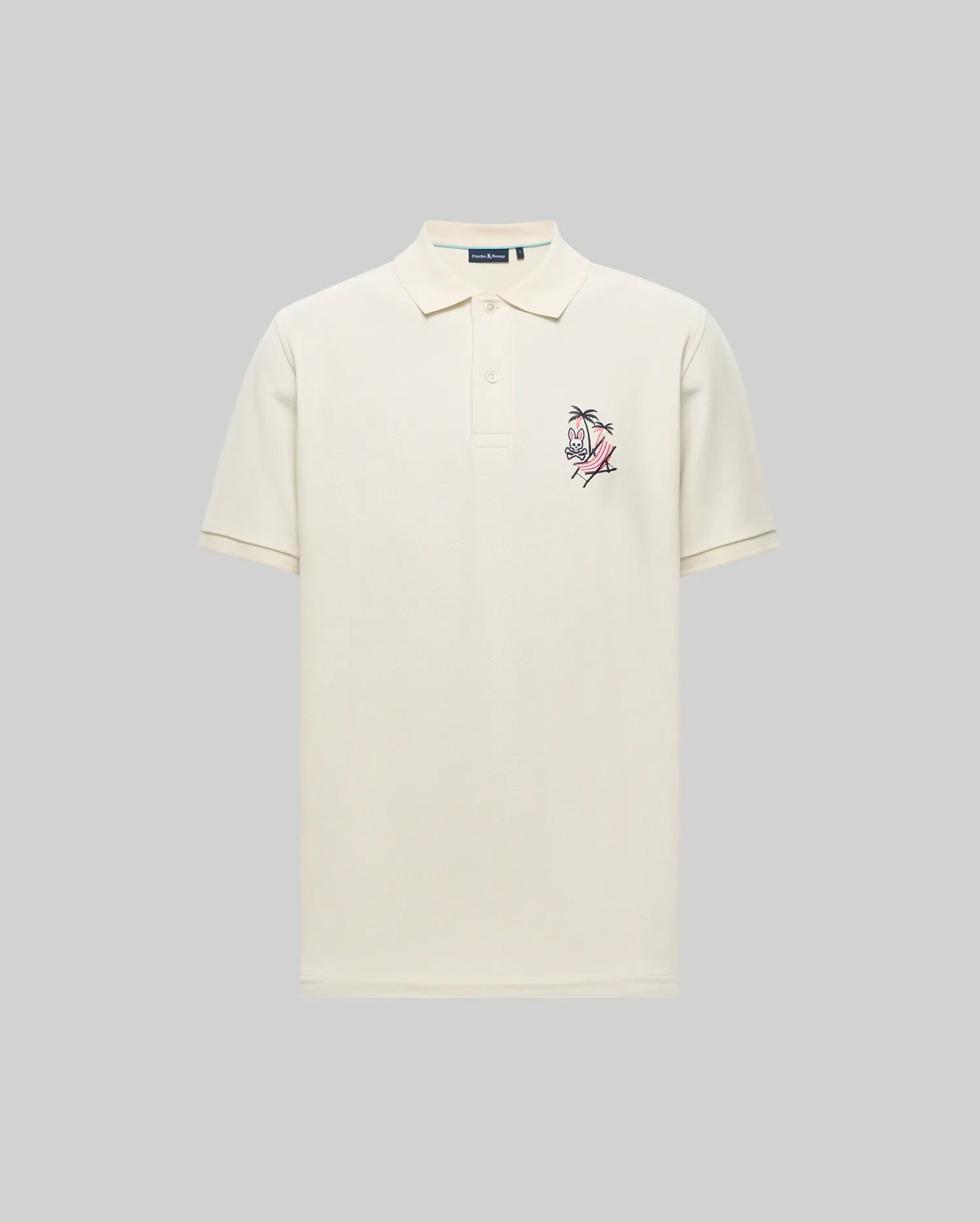 The Psycho Bunny MENS SONNY PIQUE POLO - MT0100094 is a cream Pima cotton short-sleeve polo with a collar, three buttons, and small chest embroidery, shown on a plain gray background.