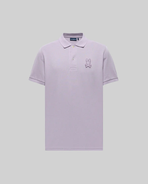 The Psycho Bunny MENS PATRICK POLO - MT0100095 is a light purple, short-sleeve 100% cotton polo with a collar, three buttons, and an embroidered cartoon bunny with a bow tie on the left chest, shown on a plain grey background.
