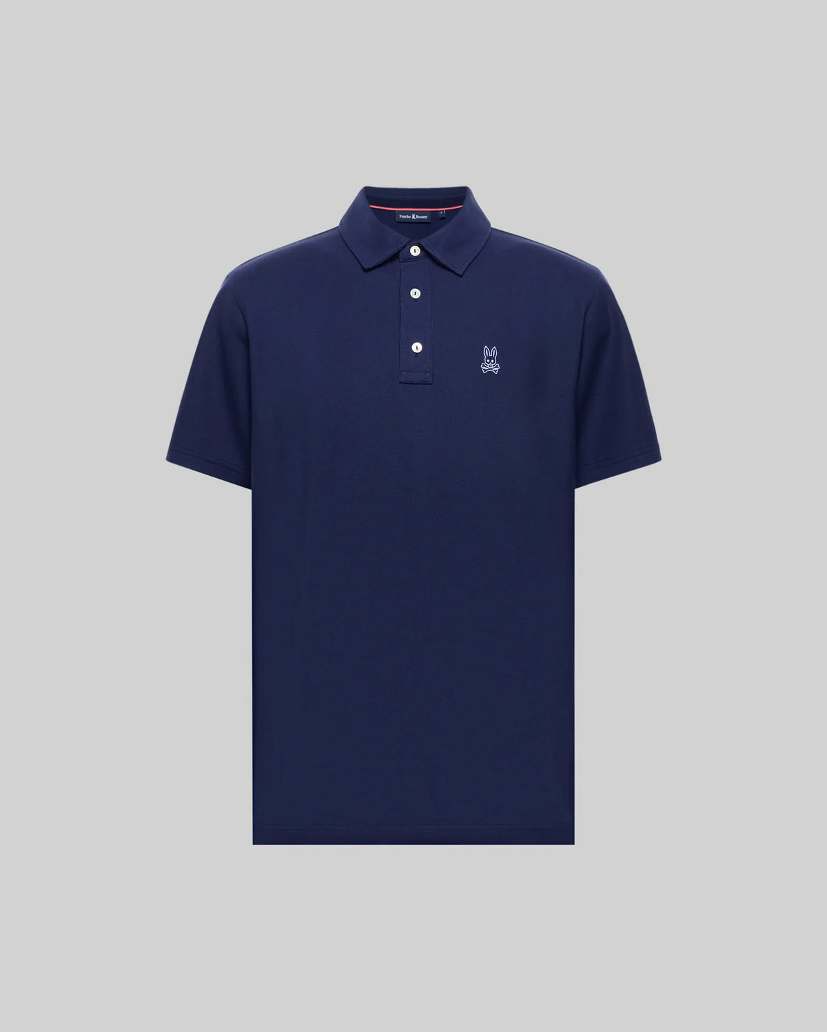 The MENS PHOENIX FASHION POLO - MT0100096 by Psycho Bunny is a navy blue, short-sleeve Pima cotton polo with a collar, three white buttons, and a small white embroidered logo on the left chest, shown on a plain gray background.