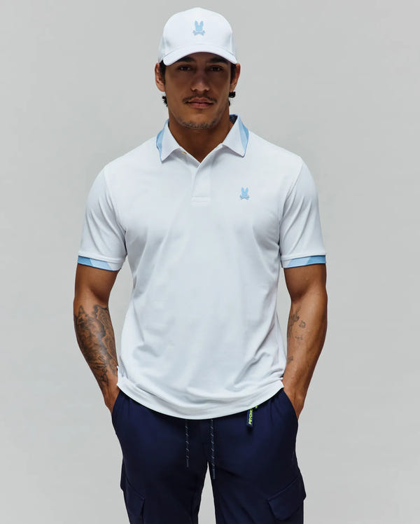 Mens Onyx Sport Polo in white performance with light blue collar/cuffs, featuring embroidered light blue Psycho Bunny chest logo, paired with white cap with light blue Psycho Bunny logo and navy cargo shorts.
