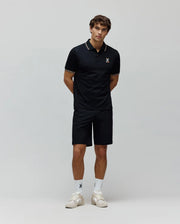 Mens Ara Pique Polo in navy, classic fit pique knit, with white and gold striped collar and cuffs, and a small embroidered multi-color Psycho Bunny skull logo on the left chest. Paired with matching navy shorts.