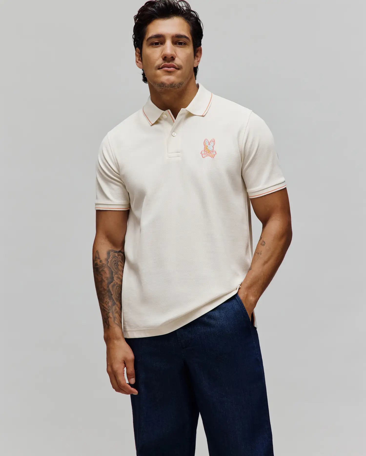 Mens Olivier Pique Polo, a cream classic fit pique polo with orange tipping on the collar and cuffs, featuring an embroidered multi-color Psycho Bunny skull logo on the left chest.