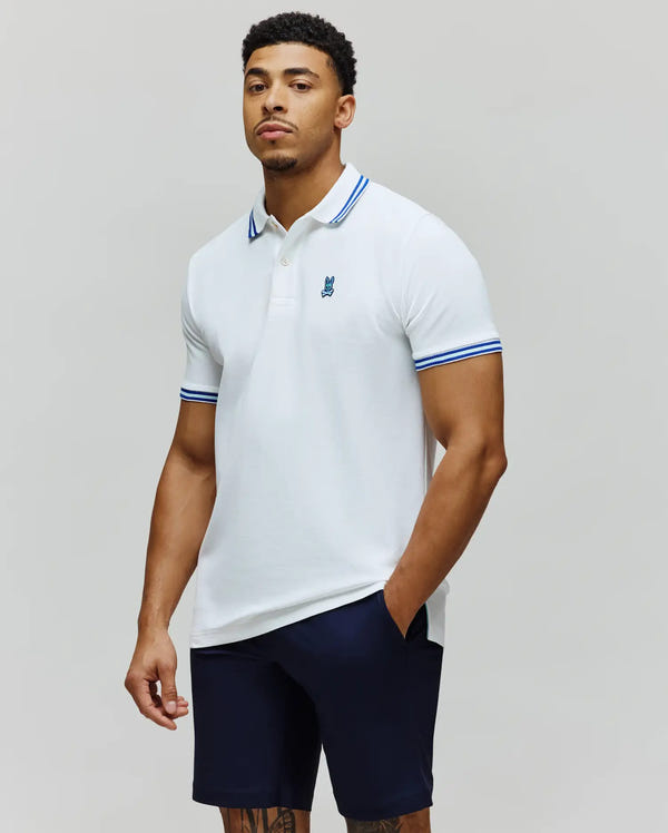 White Mens Clark Pique Polo, classic fit, with dark blue tipped collar and cuffs, featuring a small embroidered bright blue Psycho Bunny skull logo on the left chest.