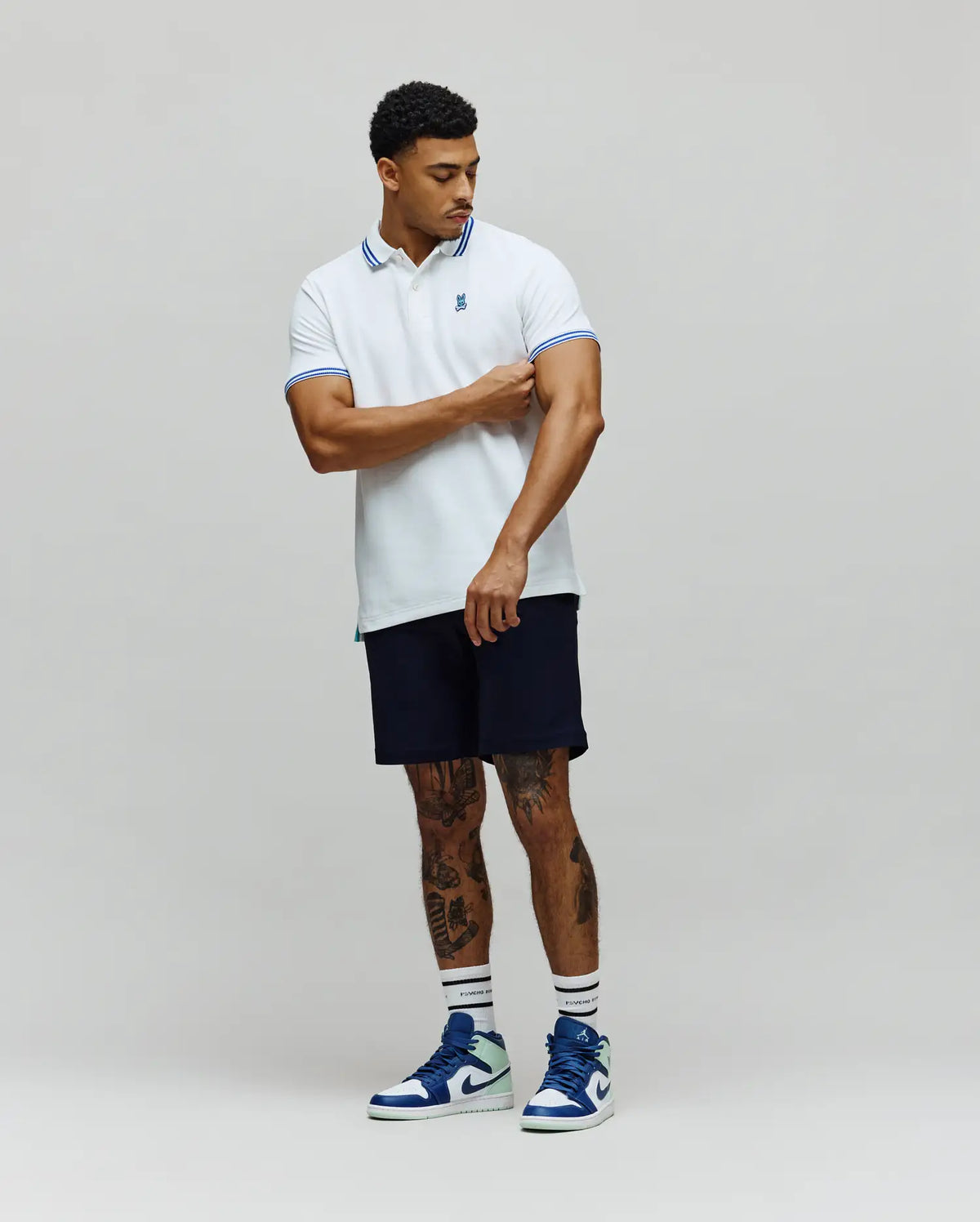 Mens Clark Pique Polo in white, featuring a classic fit, blue striped collar and cuffs, with a small embroidered Psycho Bunny skull logo on the left chest.