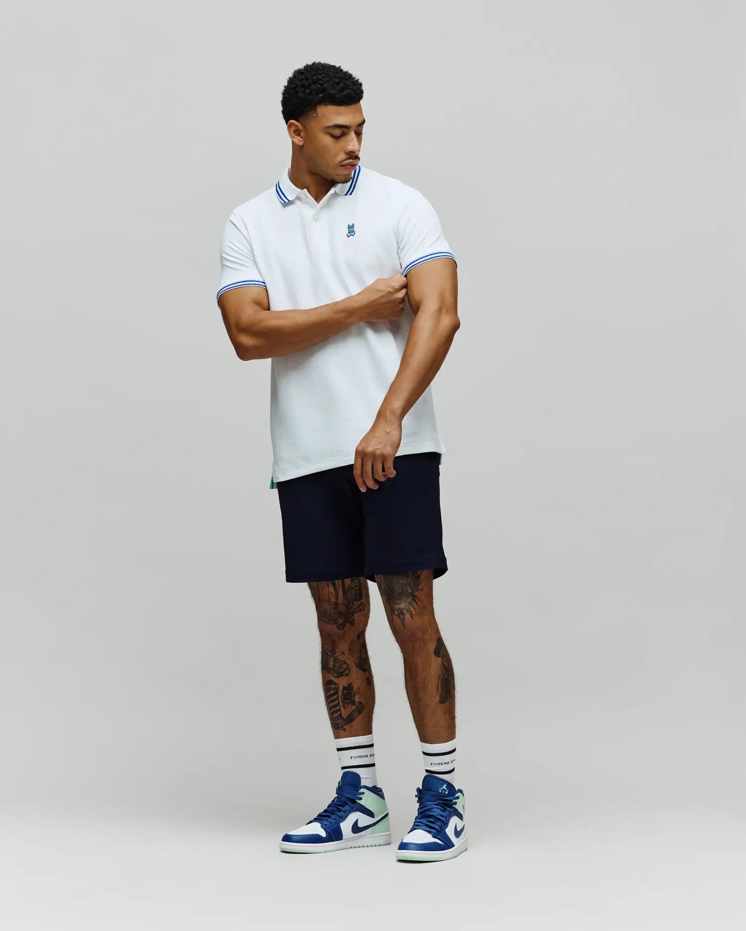Mens Clark Pique Polo in white, featuring a classic fit, blue striped collar and cuffs, with a small embroidered Psycho Bunny skull logo on the left chest.