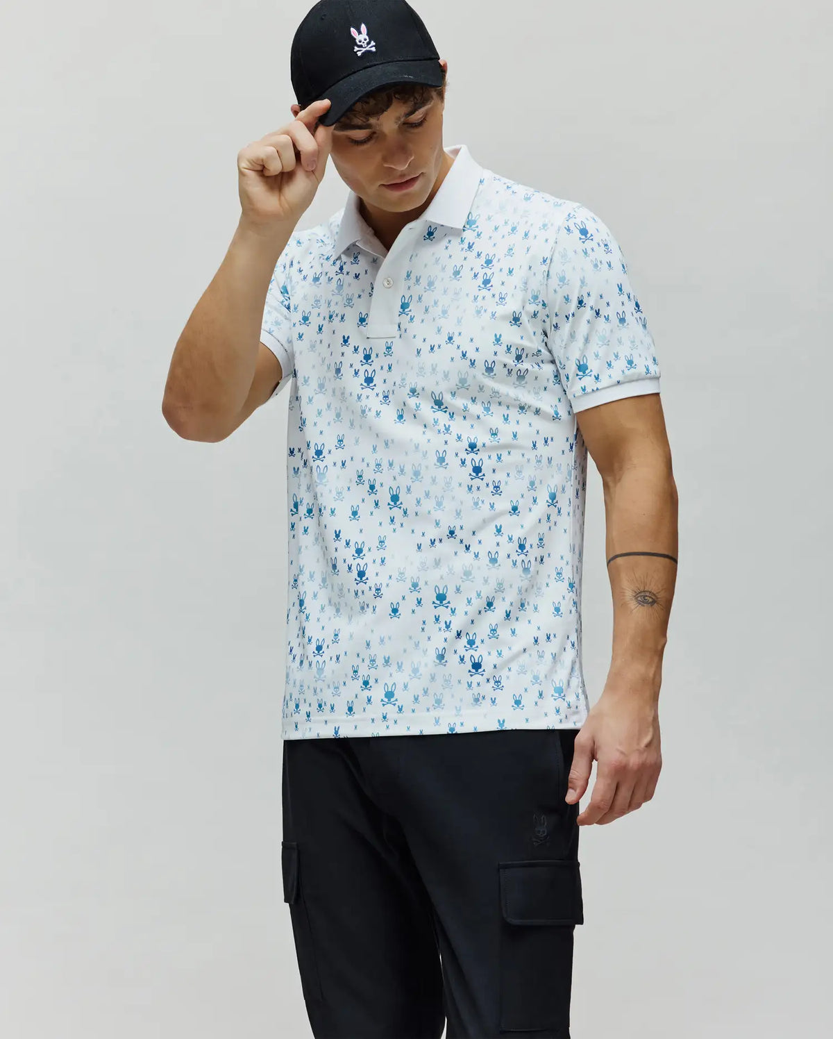 Mens Nev Sport Polo in white with an all-over gradient blue Psycho Bunny skull and crossbones print, featuring a classic fit, smooth performance fabric, and a two-button placket.