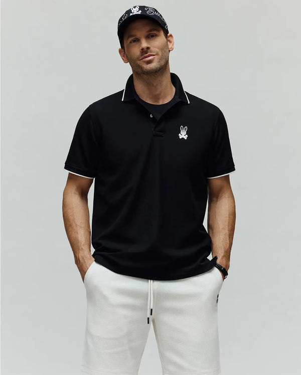 Mens Aram Pique Polo, a black classic fit pique polo with white tipping on the collar and sleeve cuffs, featuring an embroidered Psycho Bunny skull logo on the left chest.