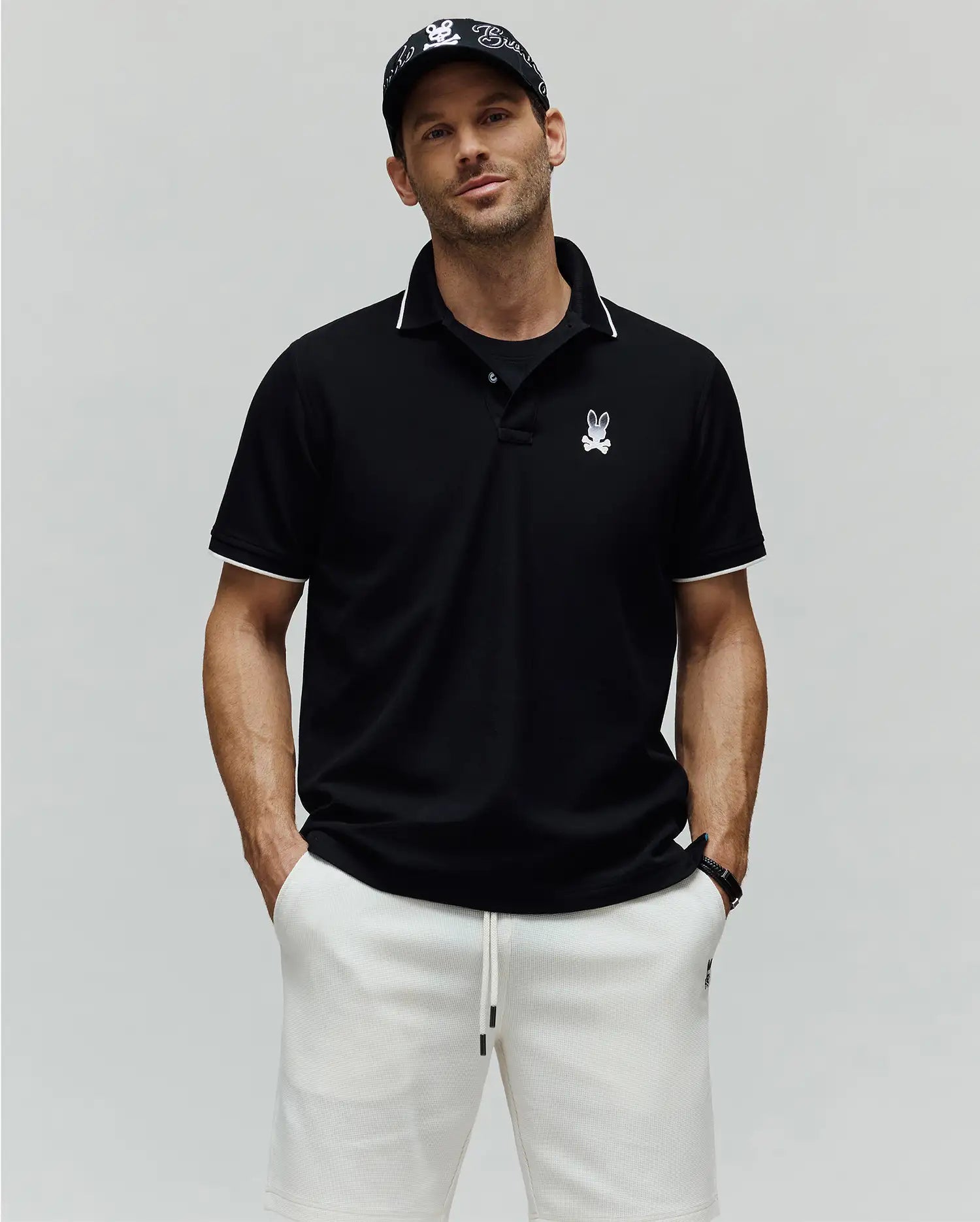 Mens Aram Pique Polo, a black classic fit pique polo with white tipping on the collar and sleeve cuffs, featuring an embroidered Psycho Bunny skull logo on the left chest.