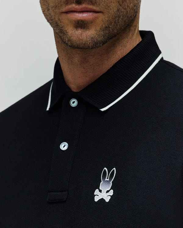 Mens Aram Pique Polo, black classic fit pique polo with white tipped ribbed collar, light blue branded buttons, and an embroidered white and grey Psycho Bunny skull logo on the left chest.