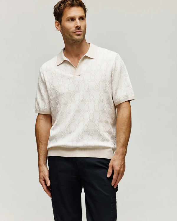 Mens Elden Johnny Collar Polo in a soft cream knit, showcasing a subtle all-over jacquard Psycho Bunny skull logo pattern, a relaxed classic fit, and refined ribbed trim on the collar, cuffs, and hem.