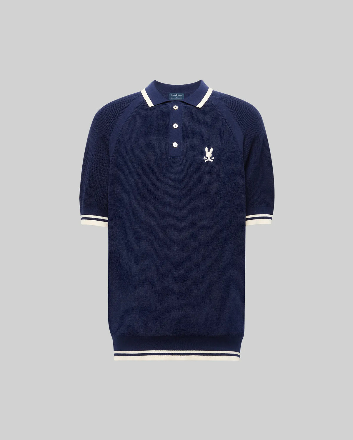 The Psycho Bunny MENS LAZARE KNIT POLO (MT0100165) is a navy short-sleeve textured knit with white trim on the collar, cuffs, and hem, a white embroidered bunny logo on the left chest, and a classic three-button placket.