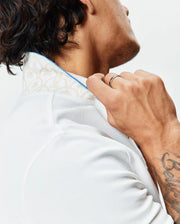Mens Brad Pique Polo in crisp white, featuring a classic fit, textured pique fabric, and a subtle beige botanical pattern on the inner collar with bright blue piping. (2)