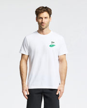 A short-haired man wears the Psycho Bunny MENS DALE GRAPHIC TEE - MT0200016, a plain white Pima cotton T-shirt with a small embroidered green logo on the chest, paired with black pants. He stands facing forward against a plain white background.