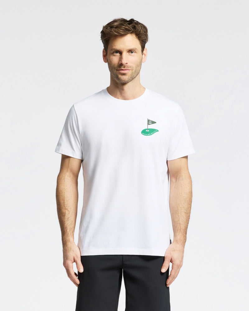 A short-haired man wears the Psycho Bunny MENS DALE GRAPHIC TEE - MT0200016, a plain white Pima cotton T-shirt with a small embroidered green logo on the chest, paired with black pants. He stands facing forward against a plain white background.