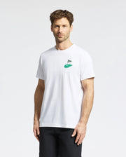 A man with short brown hair and facial hair wears a Psycho Bunny MENS DALE GRAPHIC TEE - MT0200016, a white Pima cotton T-shirt with an embroidered flag and mound logo on the chest. He stands against a plain white background, looking at the camera neutrally.