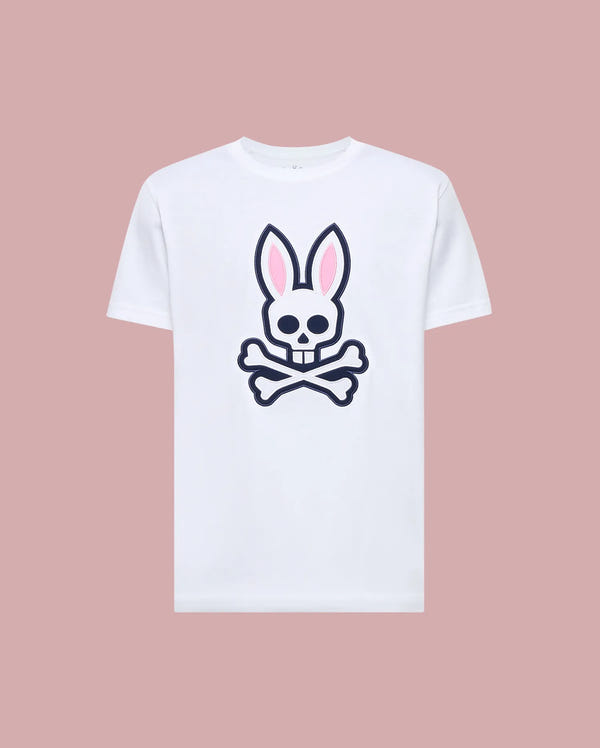 The Psycho Bunny MENS ARCHIVE BUNNY GRAPHIC TEE (MT0200031) is a white Pima cotton shirt with a bold front graphic of a skull with bunny ears and crossed bones, shown on a light pink background.
