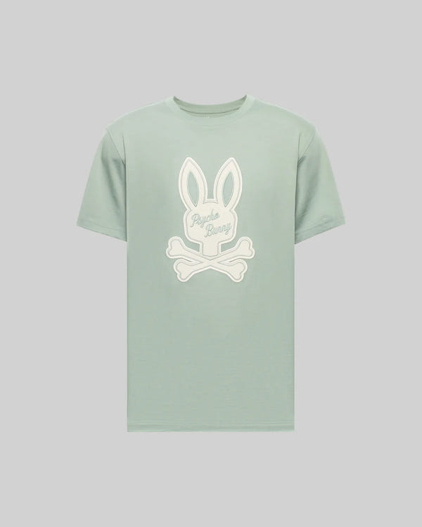 The MENS DEREK CENTER GRAPHIC TEE (MT0200048) by Psycho Bunny is a light green Pima cotton shirt with a white cartoon bunny head above crossed bones and "Psycho Bunny" script, regular fit, shown on a plain gray background.