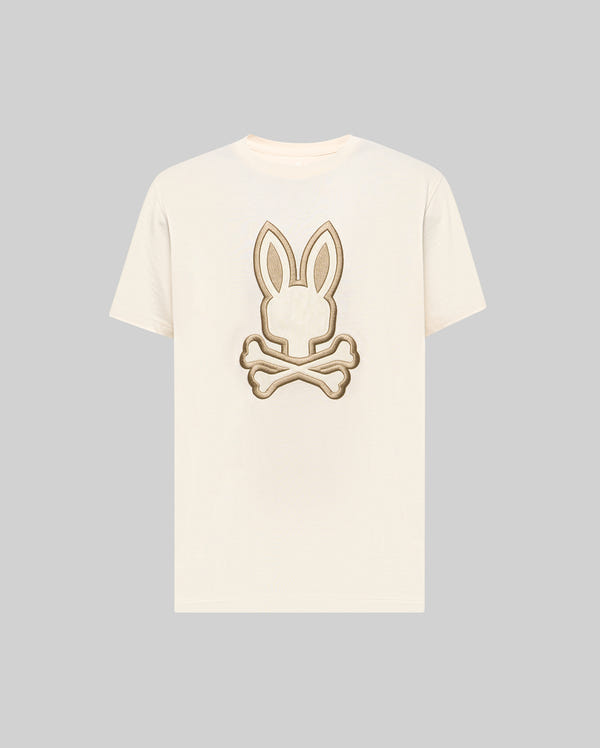 The Psycho Bunny MENS NICHOLAS EMBROIDERED TEE (MT0200054) features a cream base with a beige and brown embroidered bunny head and crossed bones motif centered on the chest.