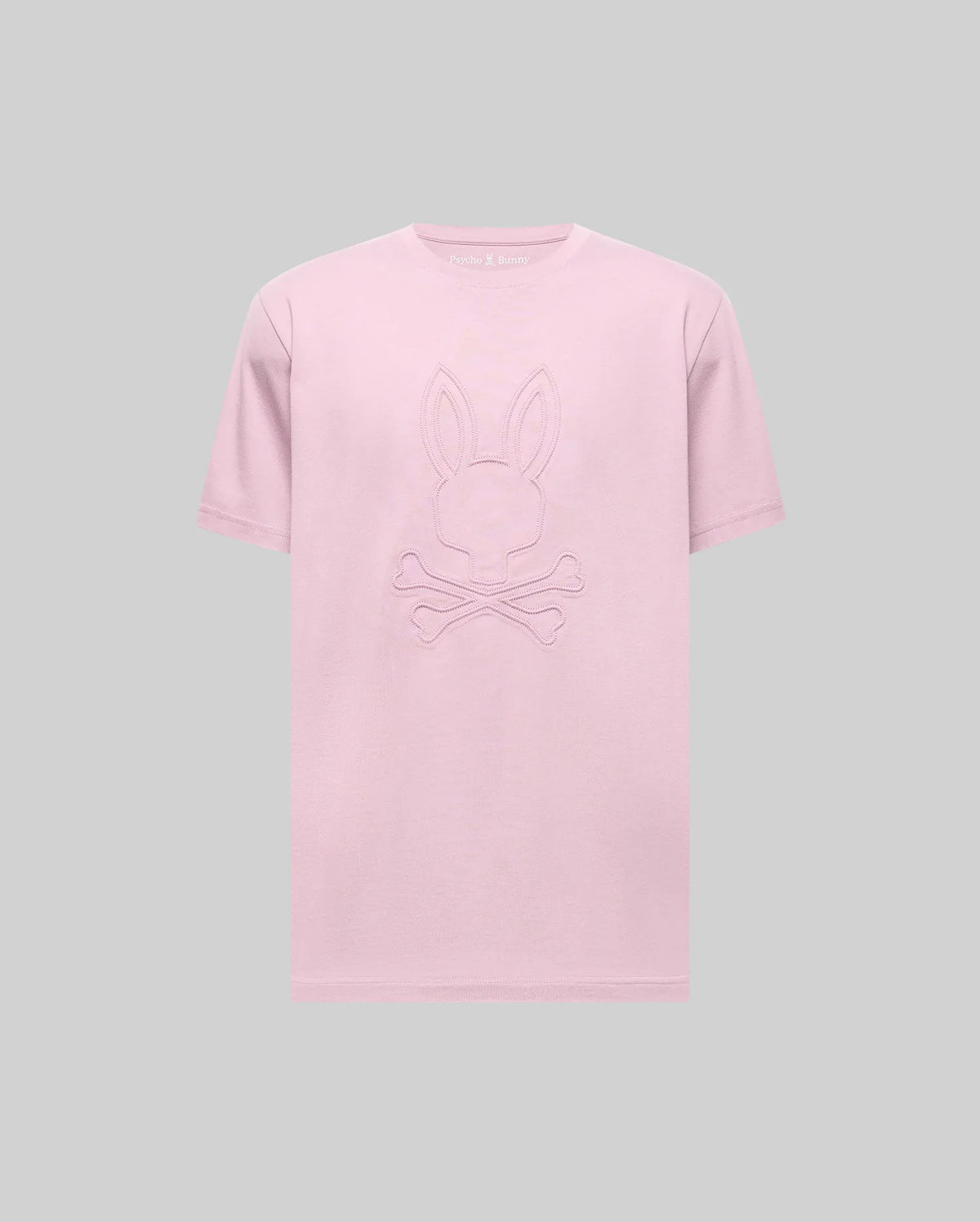 The Psycho Bunny MENS REMY GRAPHIC TEE (MT0200059) is a light pink Pima cotton shirt featuring an embossed bunny logo above crossed bones, shown on a plain gray background.