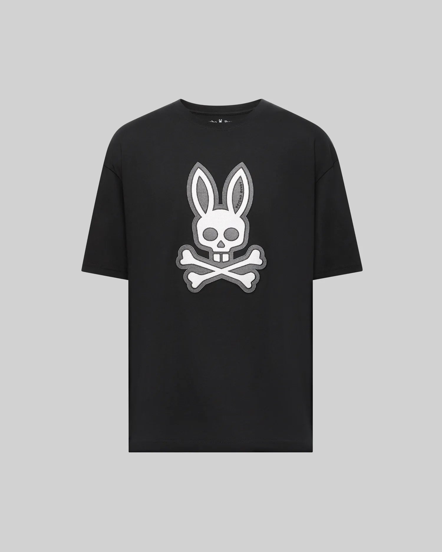 The Psycho Bunny MENS RYDER OVERSIZED TEE (MT0200062) is a black premium Pima cotton shirt with a bold white bunny head and long ears over a skull and crossbones graphic, displayed on a plain light gray background.