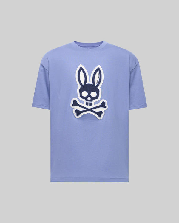 The Psycho Bunny MENS RYDER OVERSIZED TEE (MT0200062) is a light purple premium shirt with a bold front graphic of a skull with bunny ears above crossed bones, set on a plain gray background.