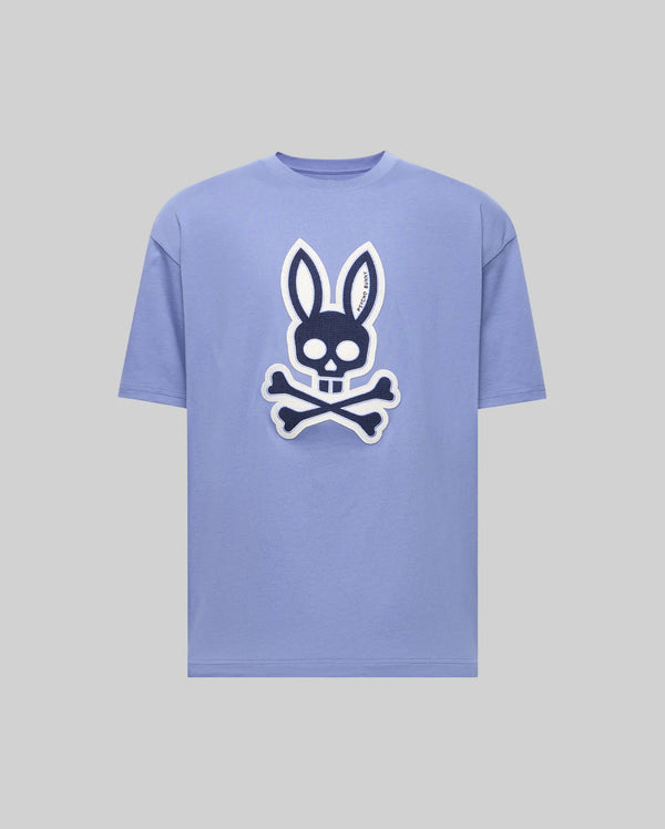 The Psycho Bunny MENS RYDER OVERSIZED TEE (MT0200062) is a light purple premium shirt with a bold front graphic of a skull with bunny ears above crossed bones, set on a plain gray background.
