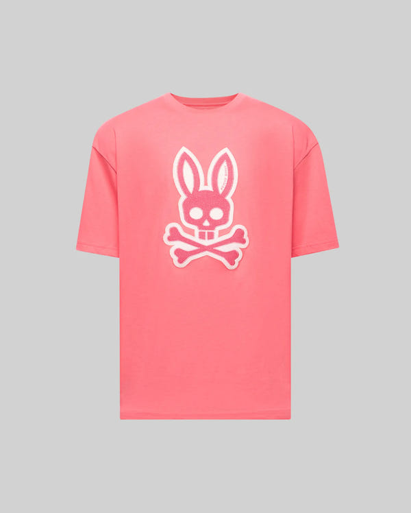 The Psycho Bunny MENS RYDER OVERSIZED TEE (MT0200062) is a pink premium shirt with a large white bunny skull and crossbones graphic on the front, shown on a plain light gray background.